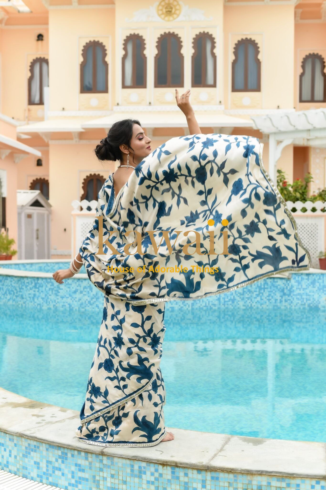 Woman wearing blue and white kalamkari saree by Kawaii posing beside a swimming pool in an elegant setting
