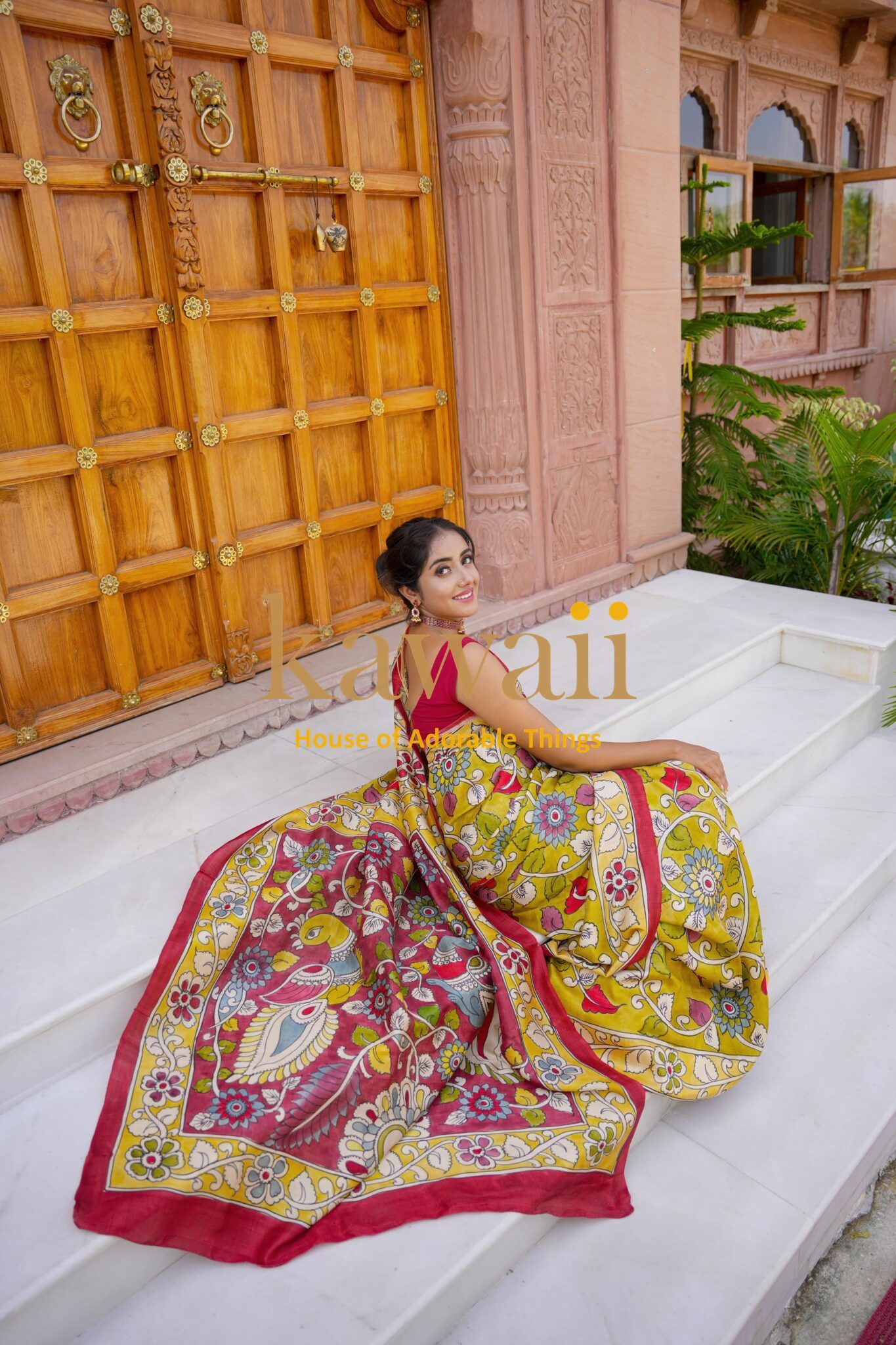 Woman wearing colorful kalamkari saree sitting on white steps with traditional wooden door background
