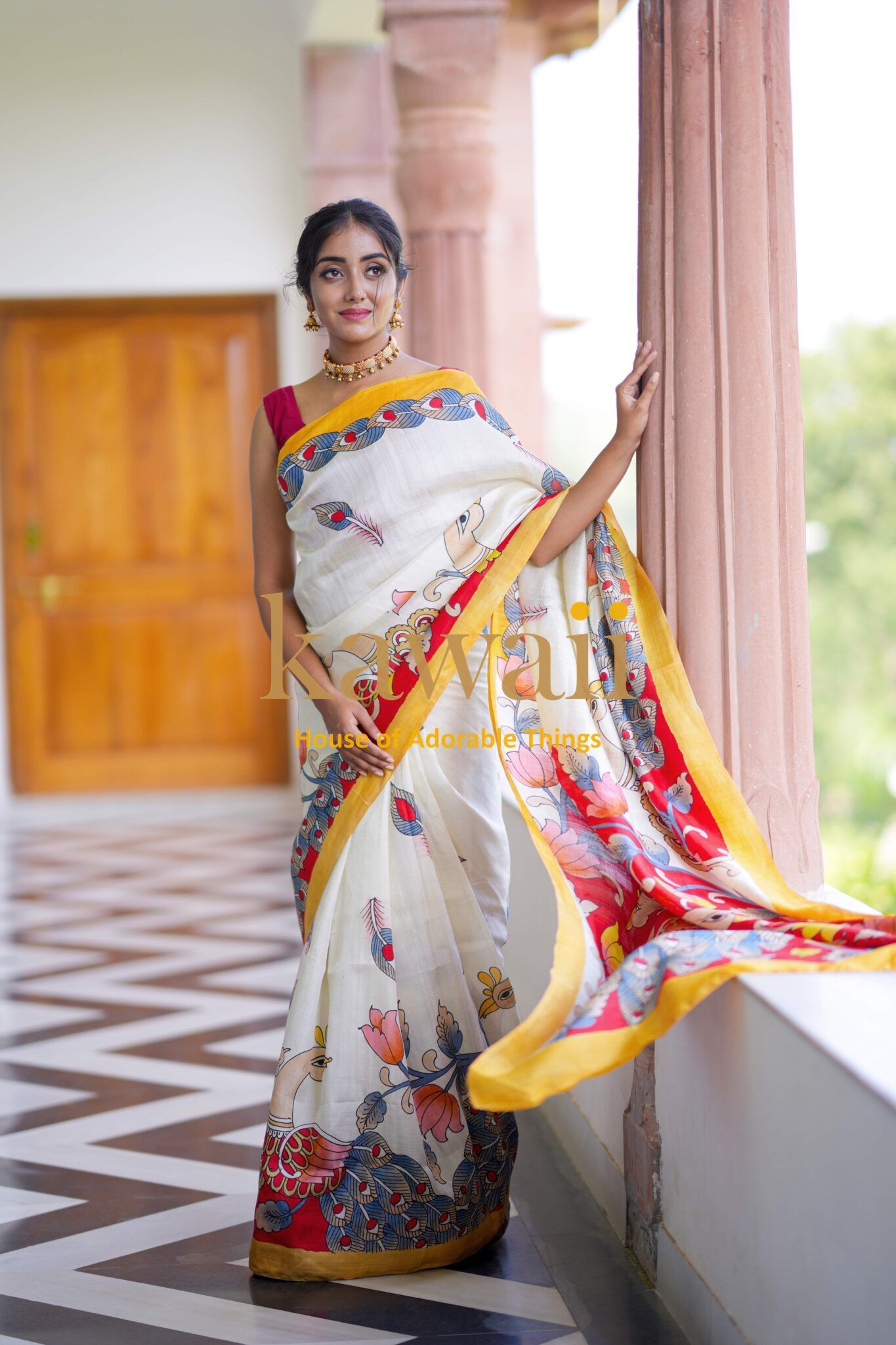 Kawaii kalamkari saree in white with colorful floral patterns and yellow border worn by a woman