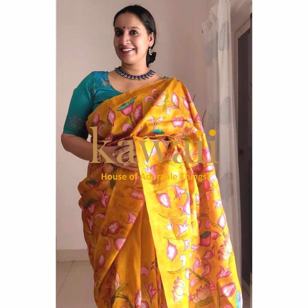 Woman wearing a yellow floral kalamkari saree paired with a teal blouse and blue necklace