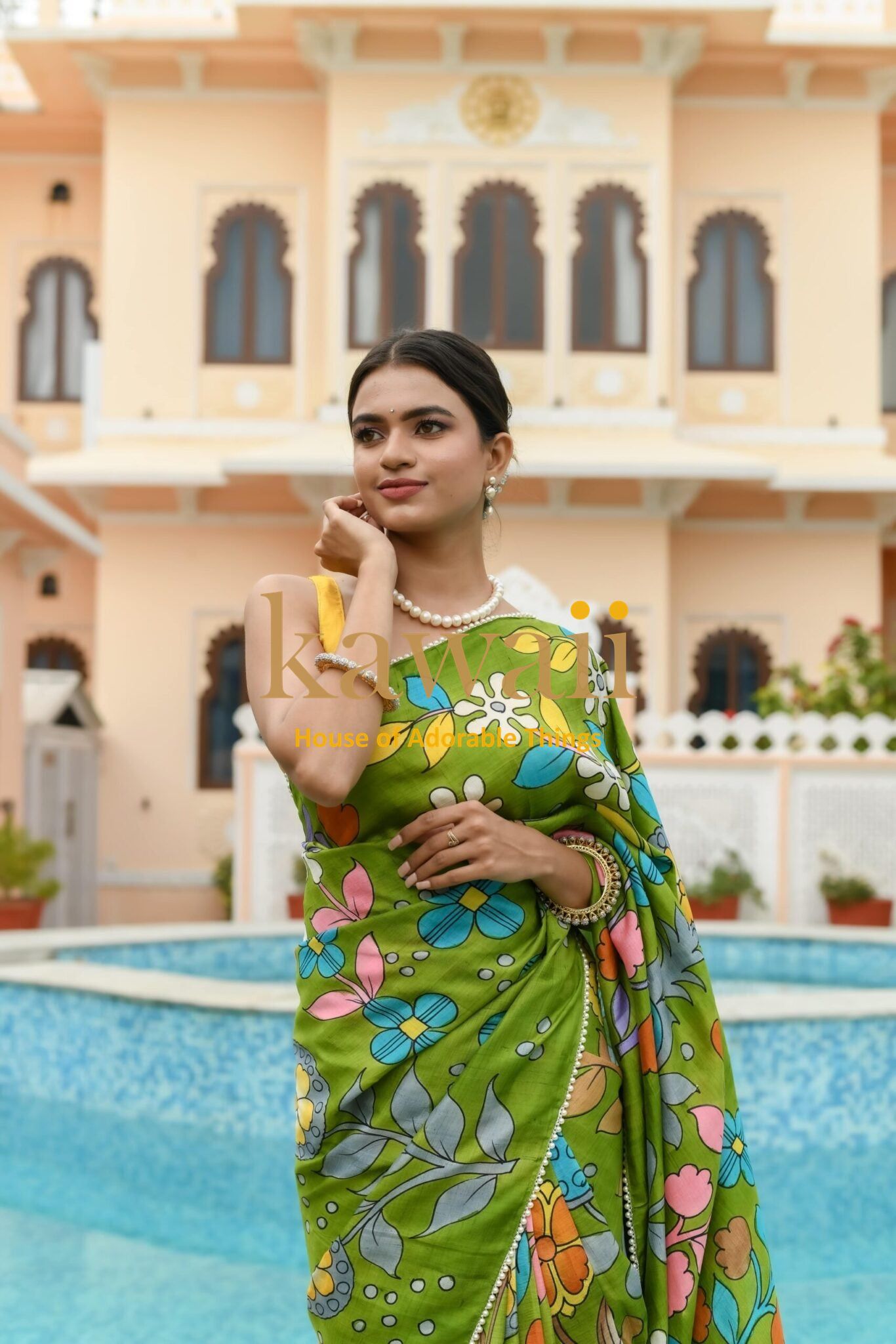 Kawaii green kalamkari saree with floral patterns worn by a woman near a pool with traditional architecture background