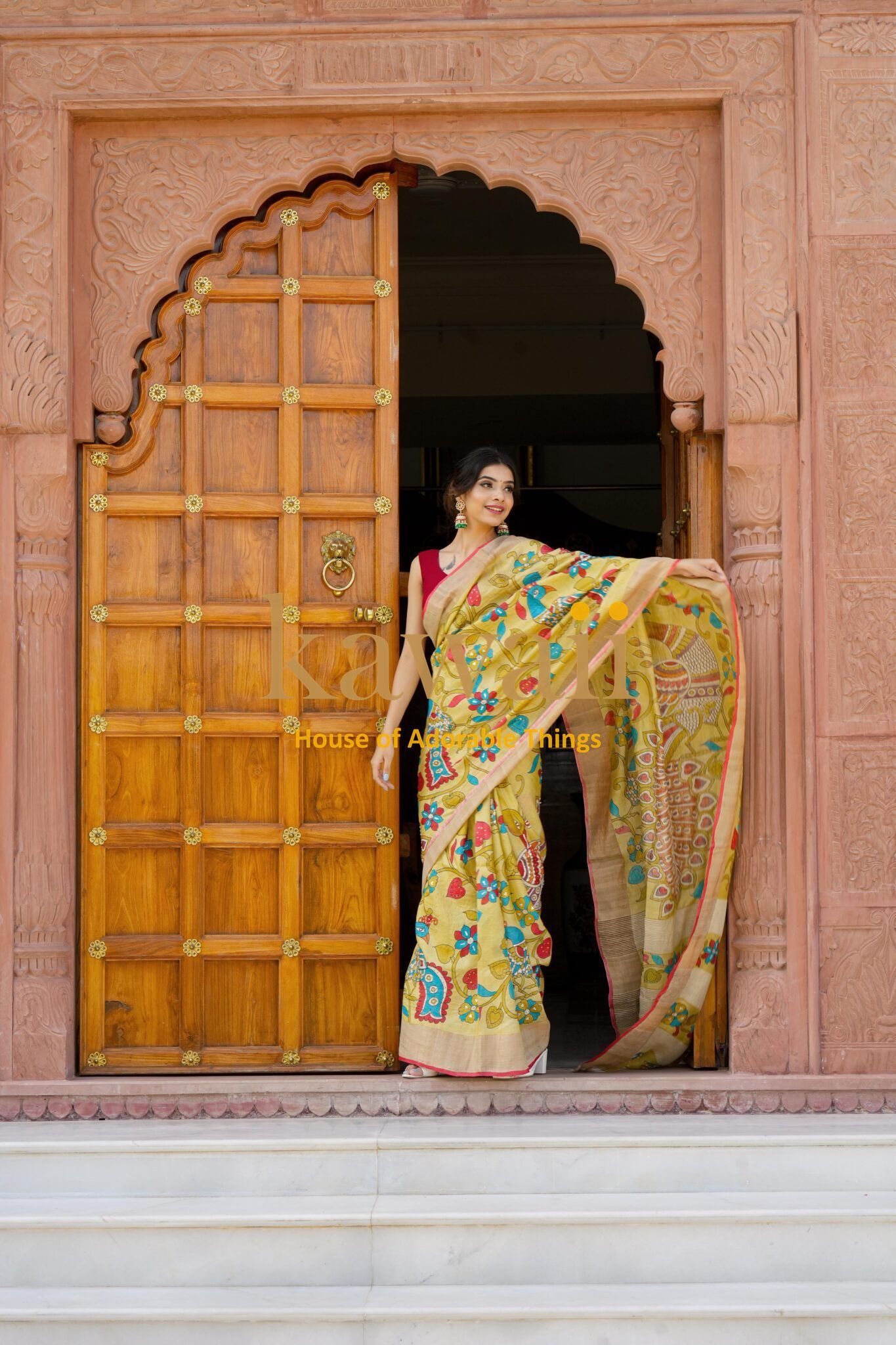 Woman wearing a colorful Kawaii kalamkari saree standing in a traditional carved wooden doorway