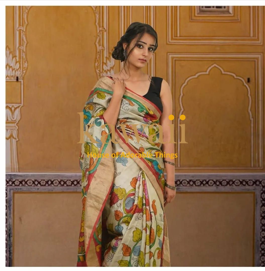 Woman wearing a colorful floral printed kalamkari saree standing against a traditional yellow wall