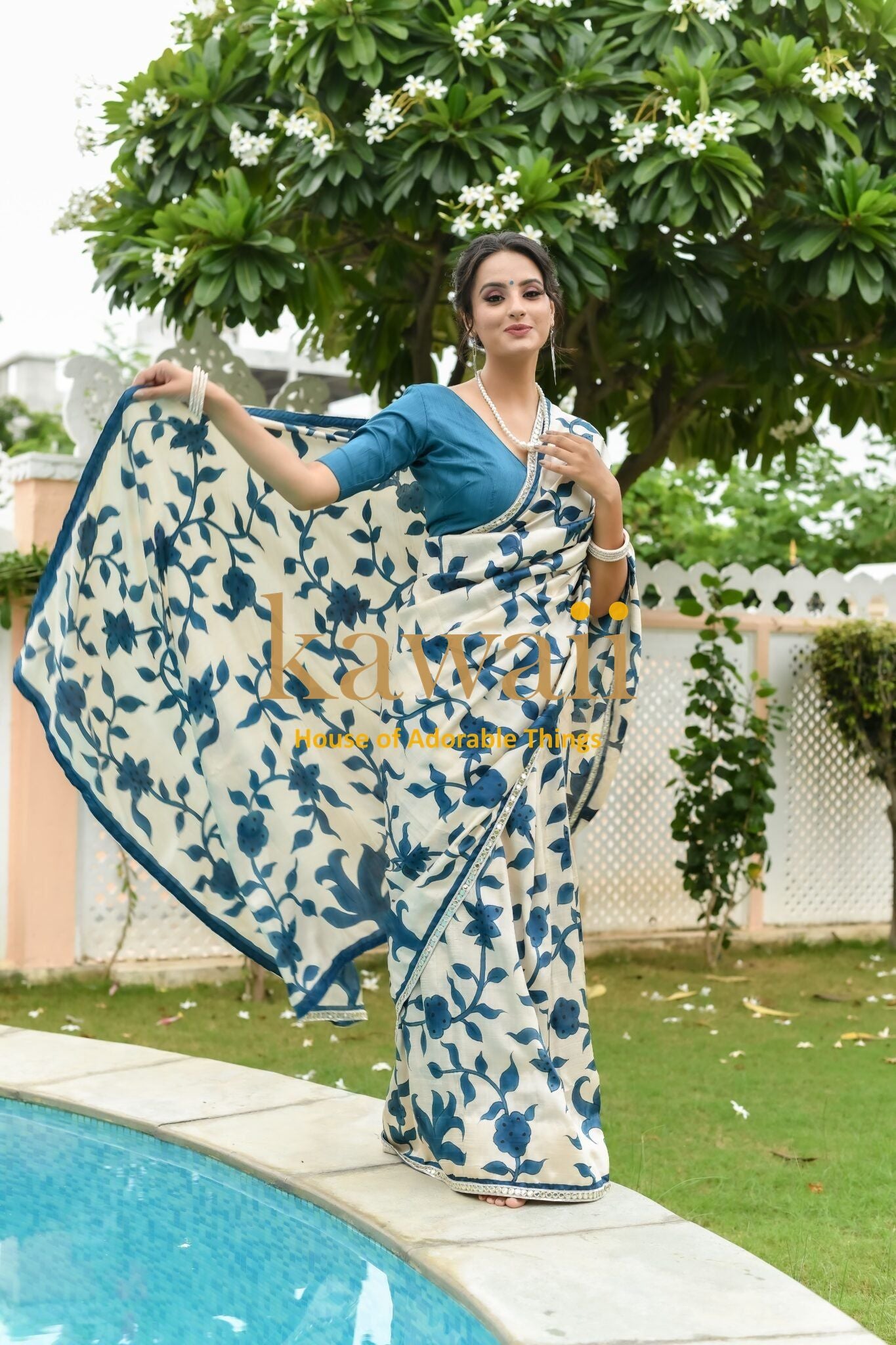 Woman wearing blue and white floral print kalamkari saree by Kawaii posing outdoors near pool