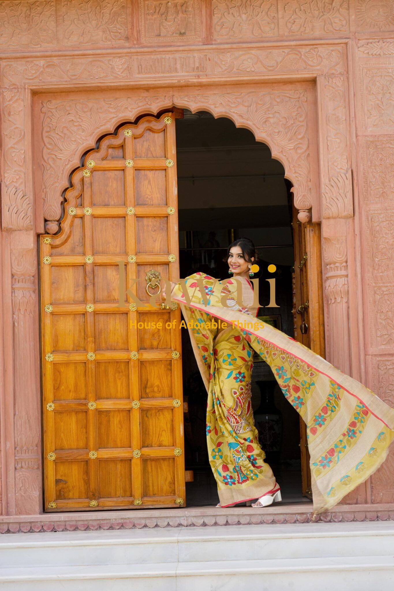 Kawaii kalamkari saree with colorful floral patterns worn by woman standing at ornate wooden door