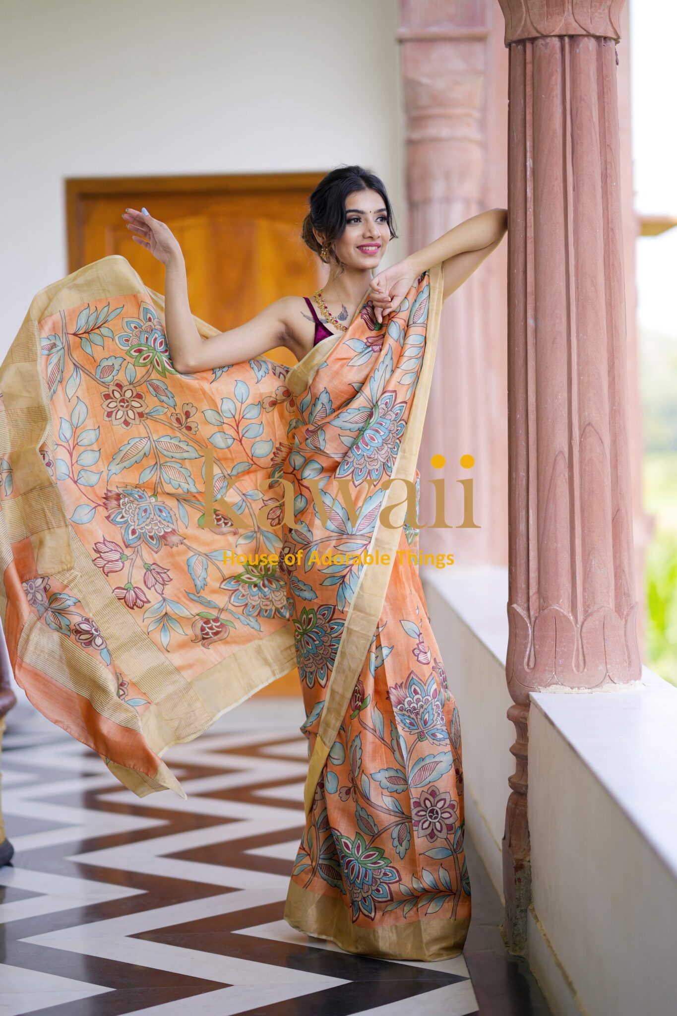 Kawaii orange floral patterned kalamkari saree worn by woman with flowing fabric in a bright setting