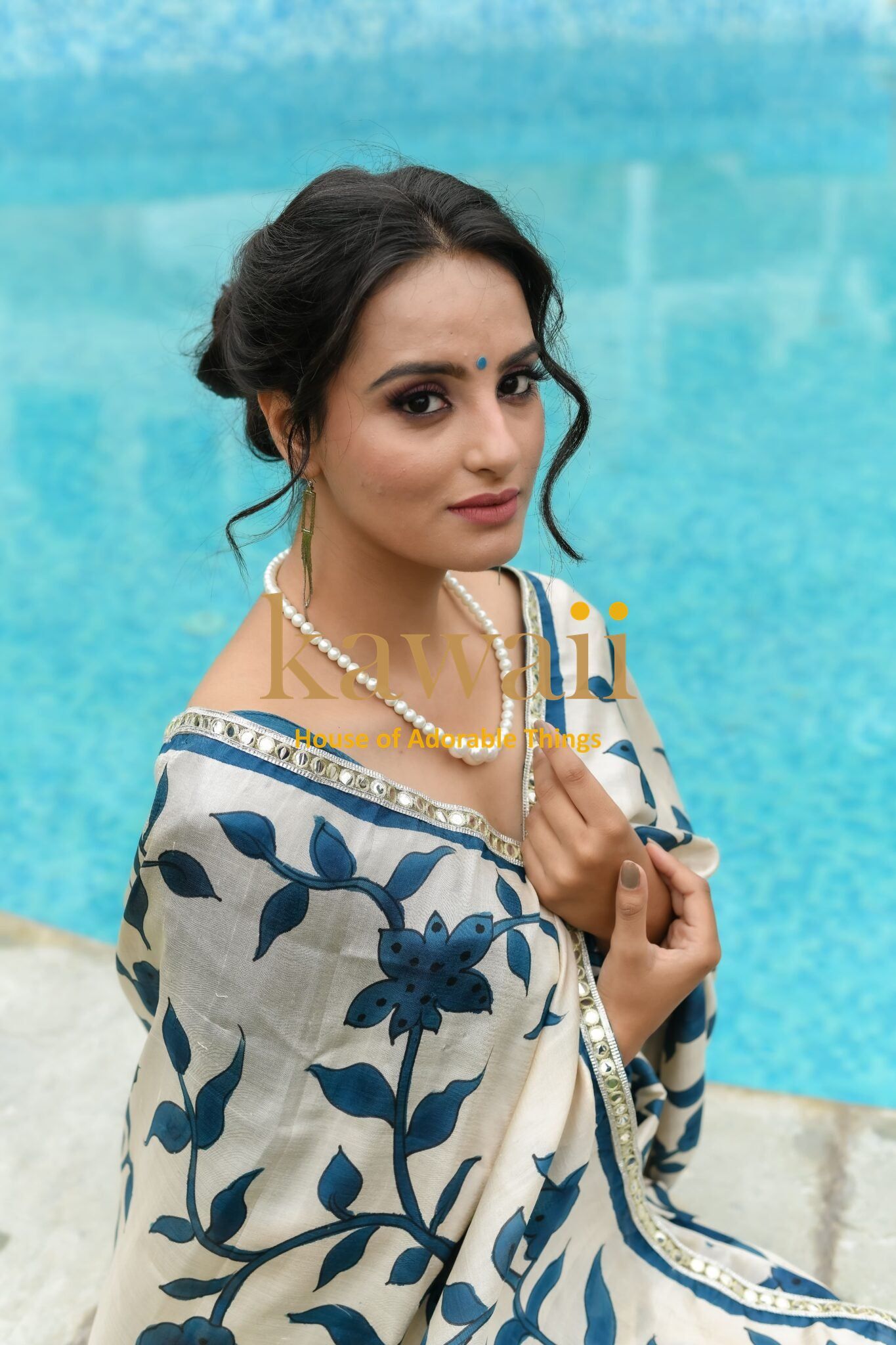 Woman wearing a Kawaii kalamkari saree with blue floral patterns sitting by the poolside