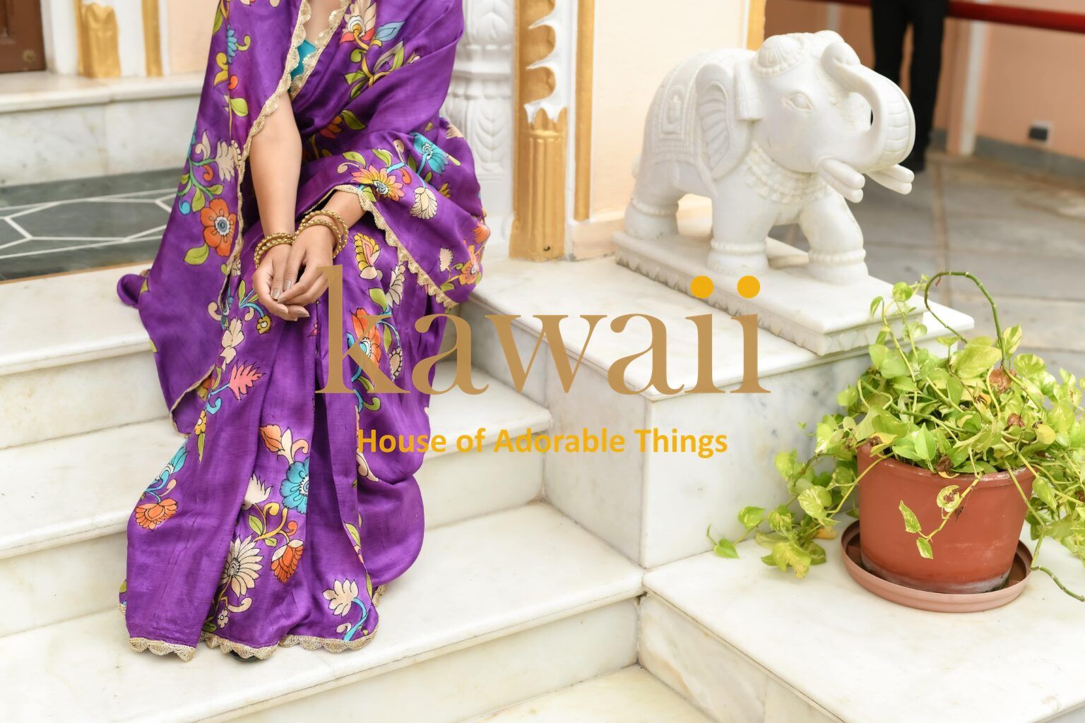 Kawaii purple kalamkari saree with colorful floral patterns worn by a seated woman indoors