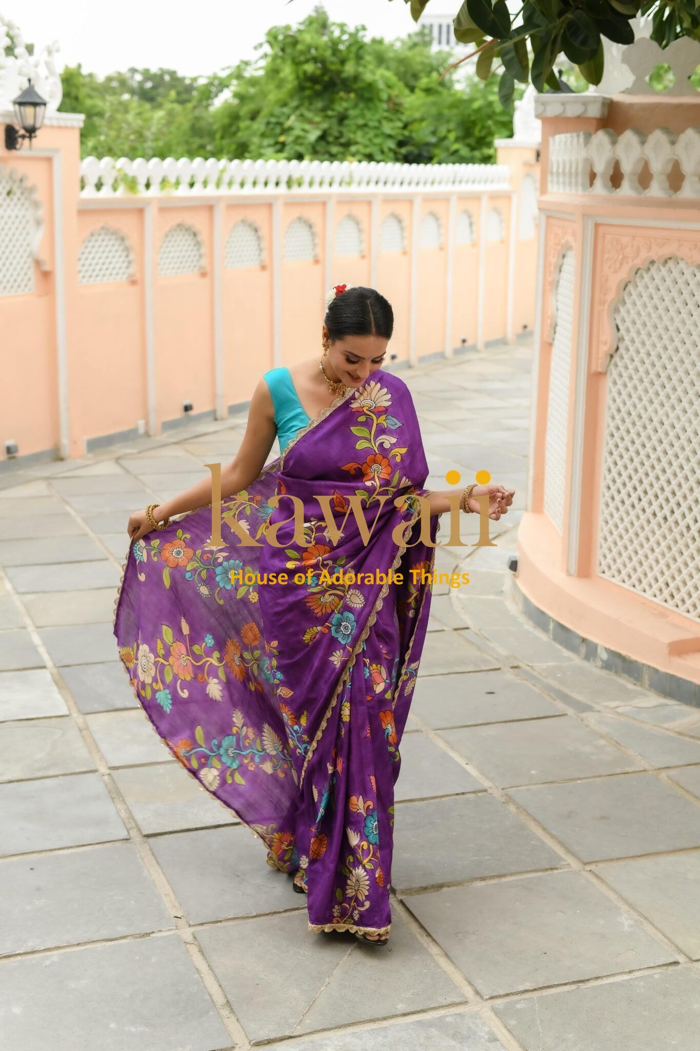 Woman wearing a purple floral kalamkari saree by Kawaii in an outdoor courtyard setting