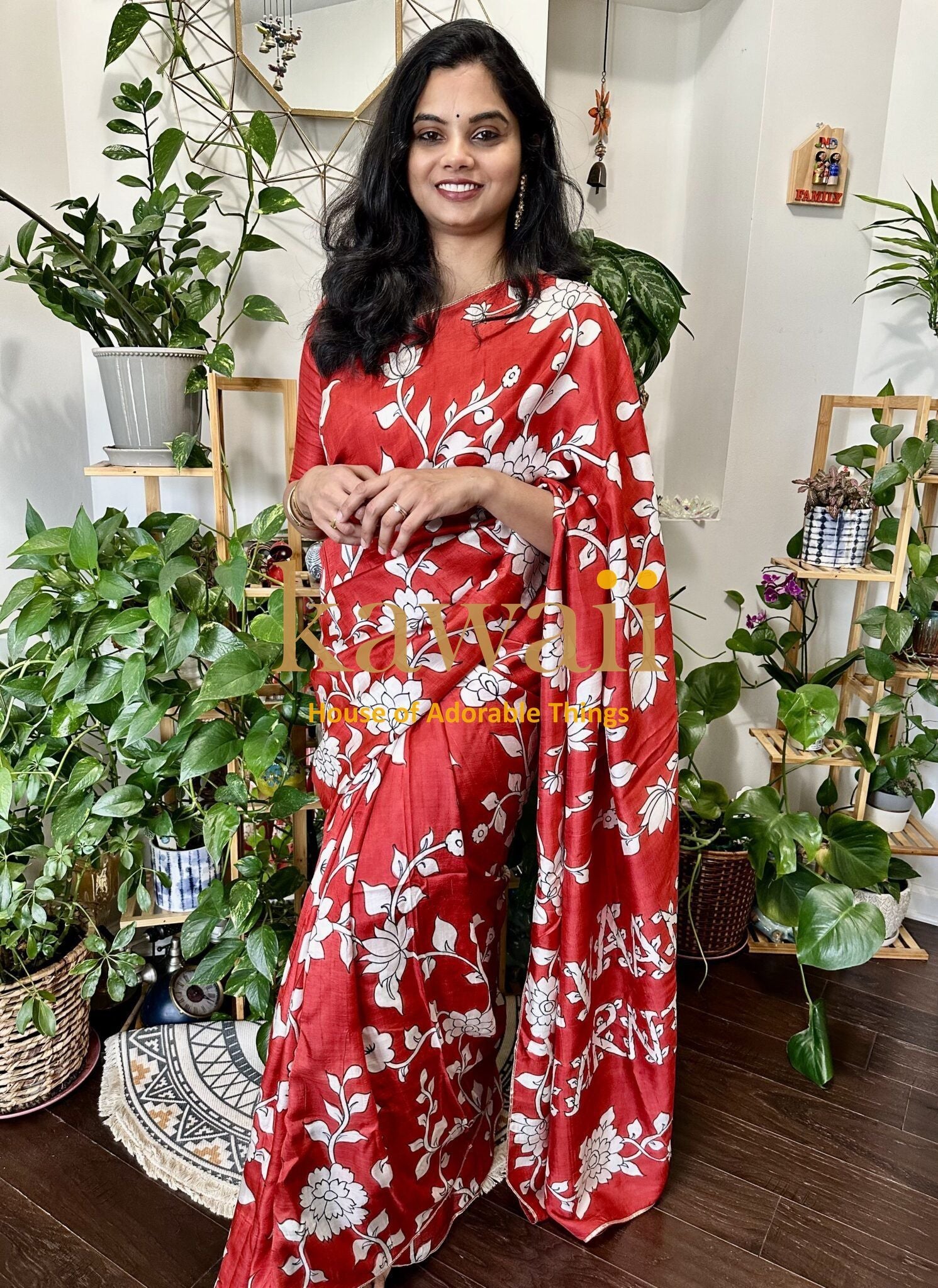 Kawaii red kalamkari saree with white floral print worn by woman standing among green indoor plants