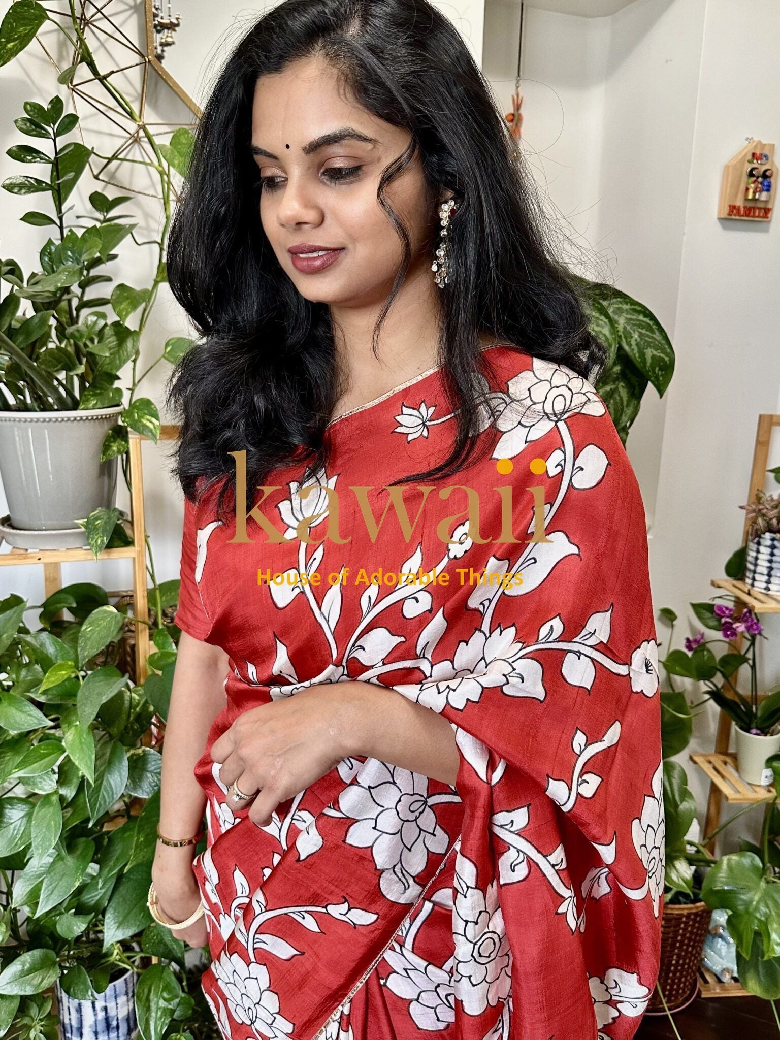 Woman wearing a red kalamkari saree with white floral patterns by Kawaii surrounded by indoor plants
