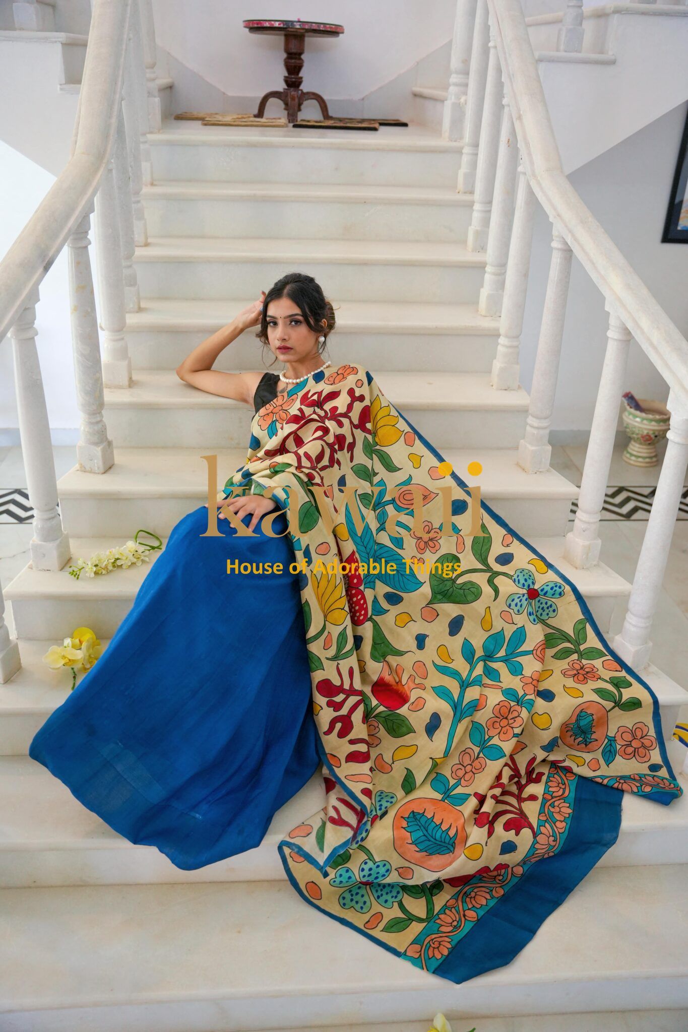 Kawaii kalamkari saree featuring vibrant floral patterns with a blue base worn by a model sitting on white stairs