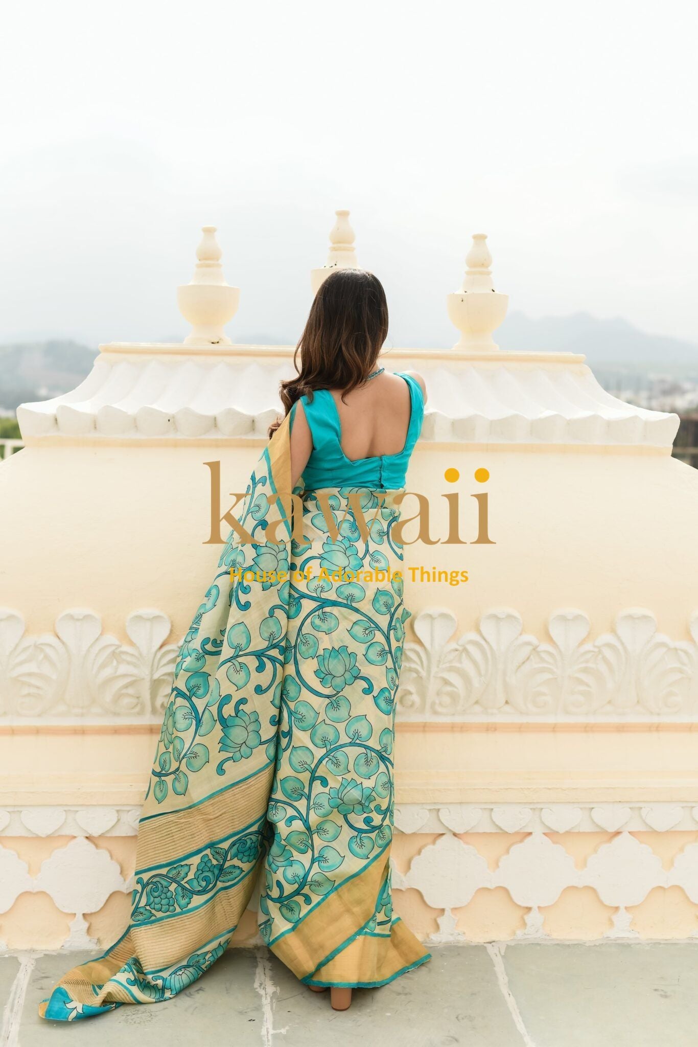 Woman wearing teal and beige Kawaii kalamkari saree with intricate floral patterns outdoors