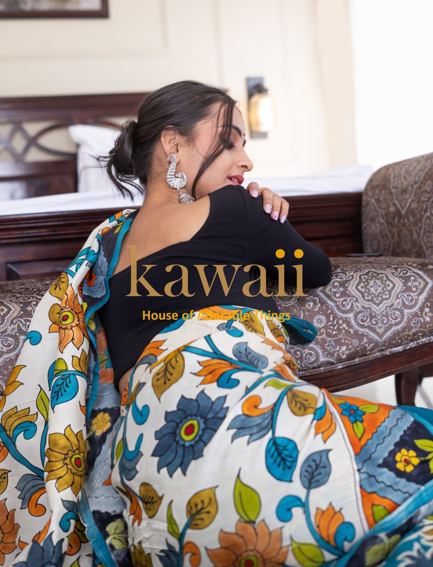 Woman wearing colorful Kawaii kalamkari saree with floral and leaf patterns sitting indoors