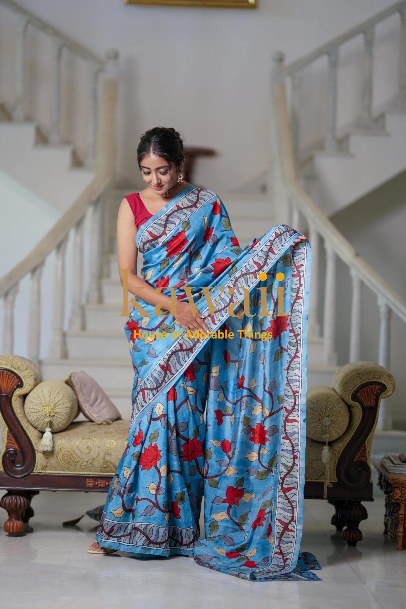 Kawaii kalamkari saree in blue with red floral patterns worn by woman standing on staircase