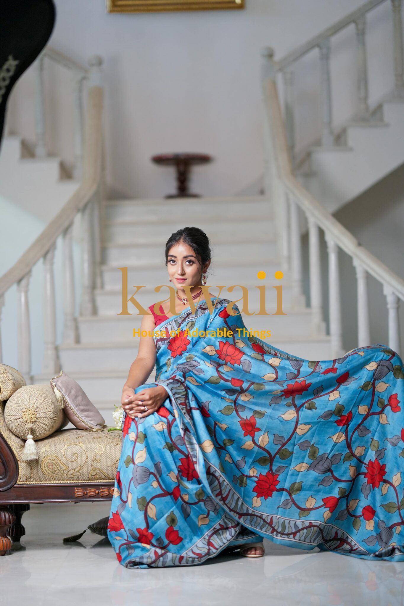 Kawaii blue kalamkari saree with red floral patterns worn by a seated woman on stairs