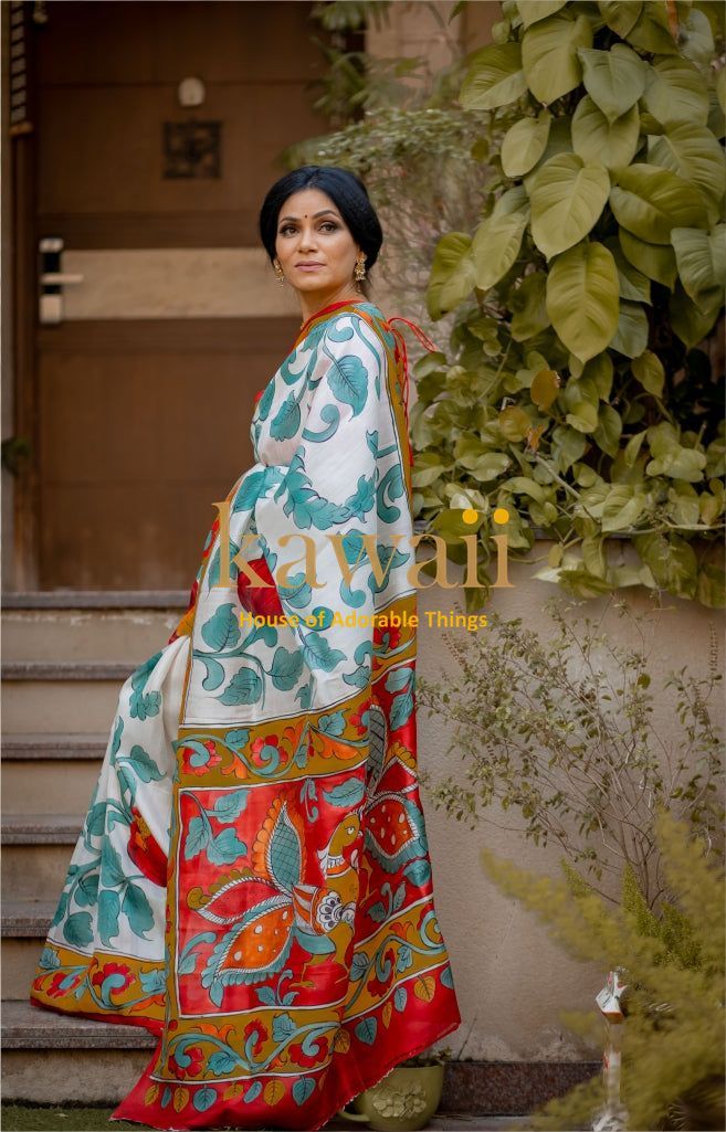Woman wearing colorful Kalamkari saree with traditional floral and leaf patterns sitting outdoors