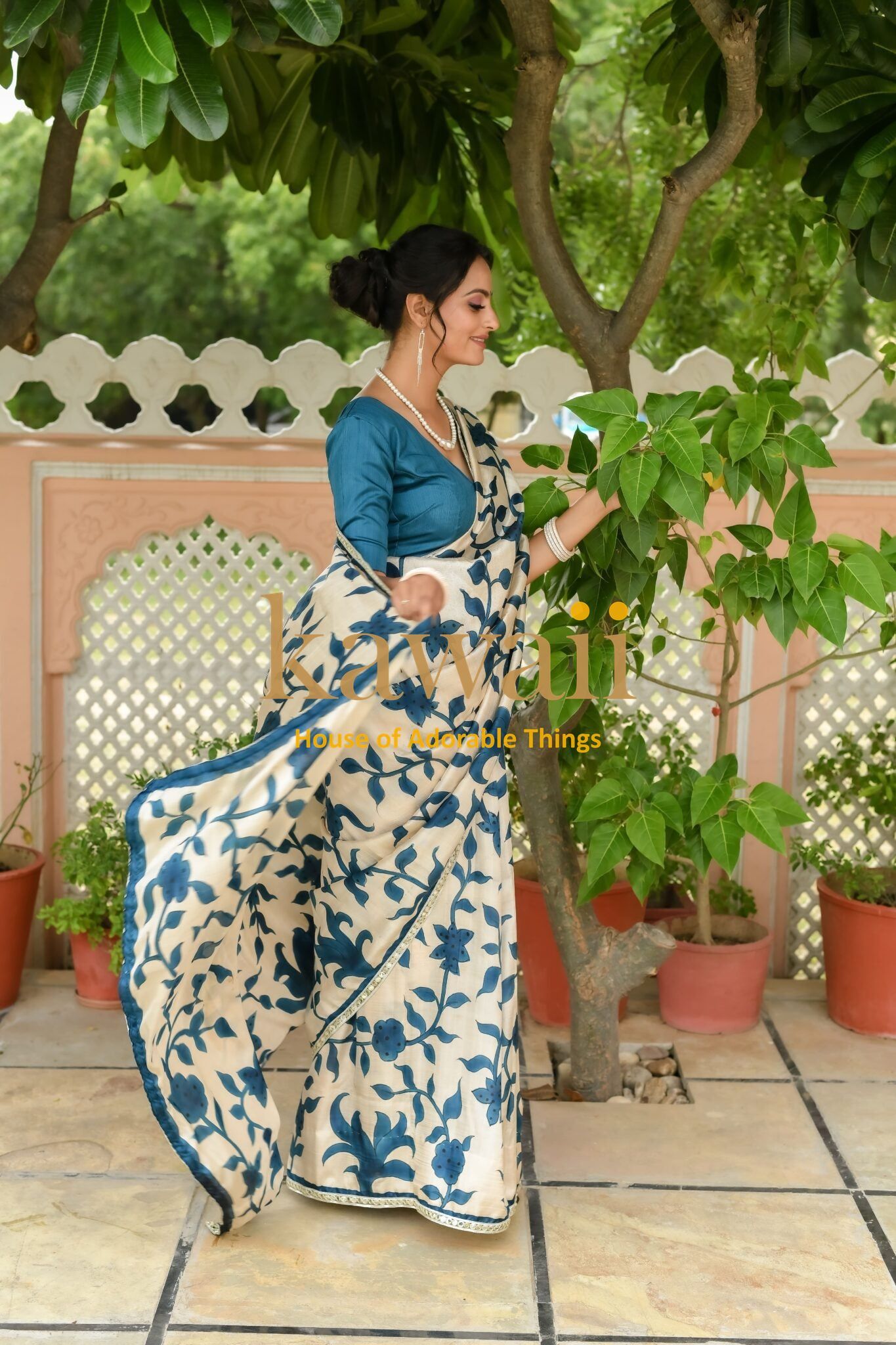 Woman wearing a blue and white floral kalamkari saree by Kawaii in an outdoor garden setting