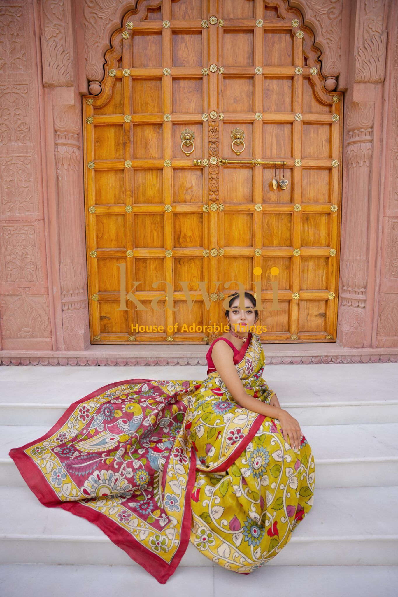 Woman wearing a colorful Kawaii kalamkari saree sitting on white steps with traditional wooden door background