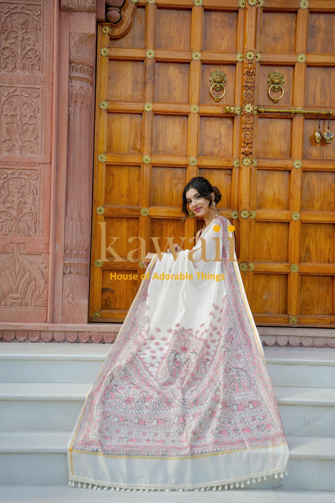 Woman wearing elegant white and pink Madhubani saree by Kawaii standing in front of wooden door