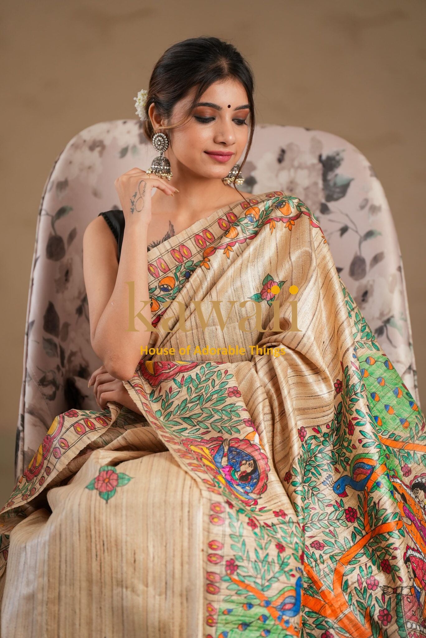 Kawaii madhubani saree with intricate floral and peacock design worn by a woman sitting on a floral chair
