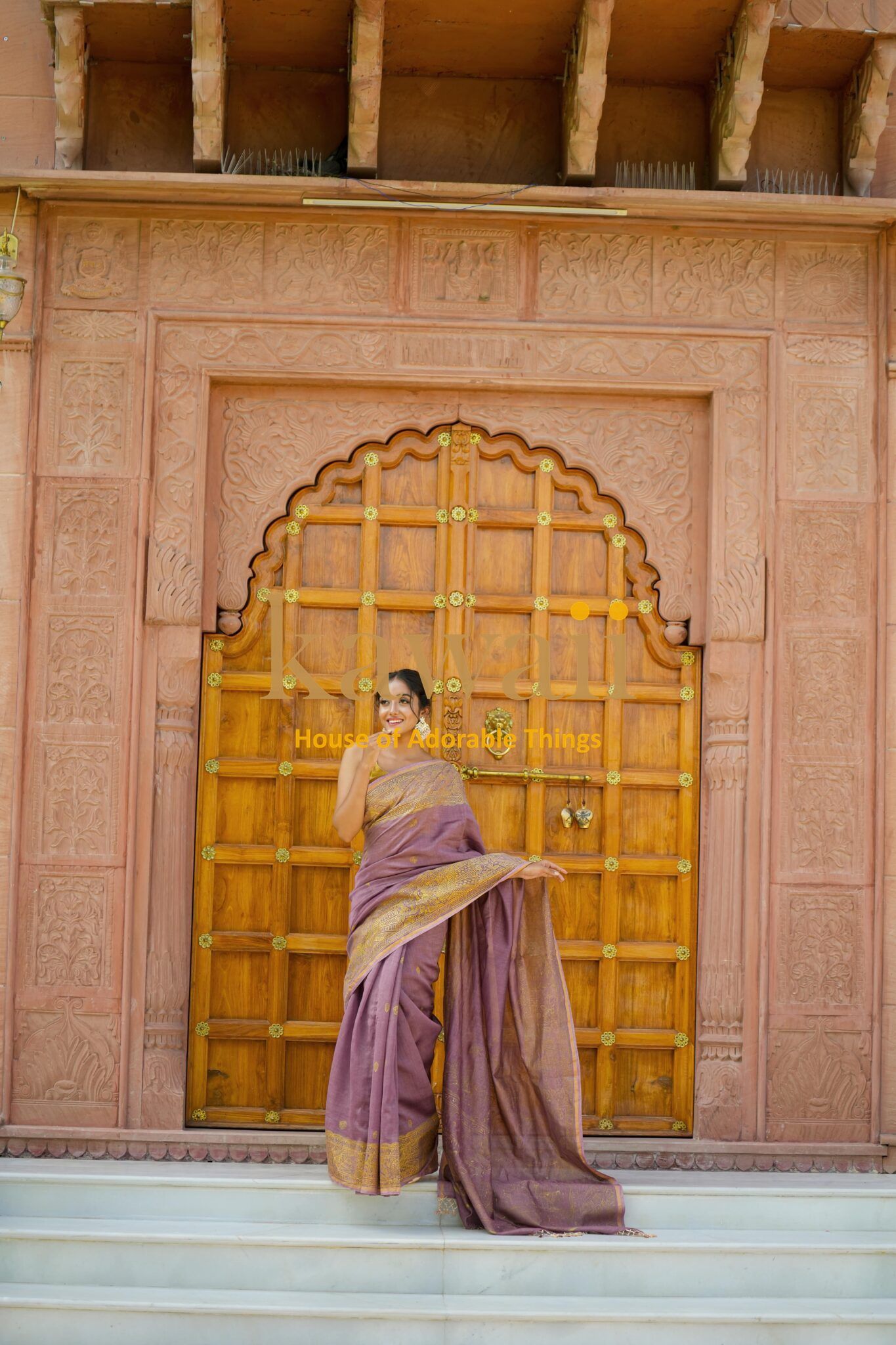 Woman wearing purple and gold Kawaii madhubani saree standing in front of carved wooden door