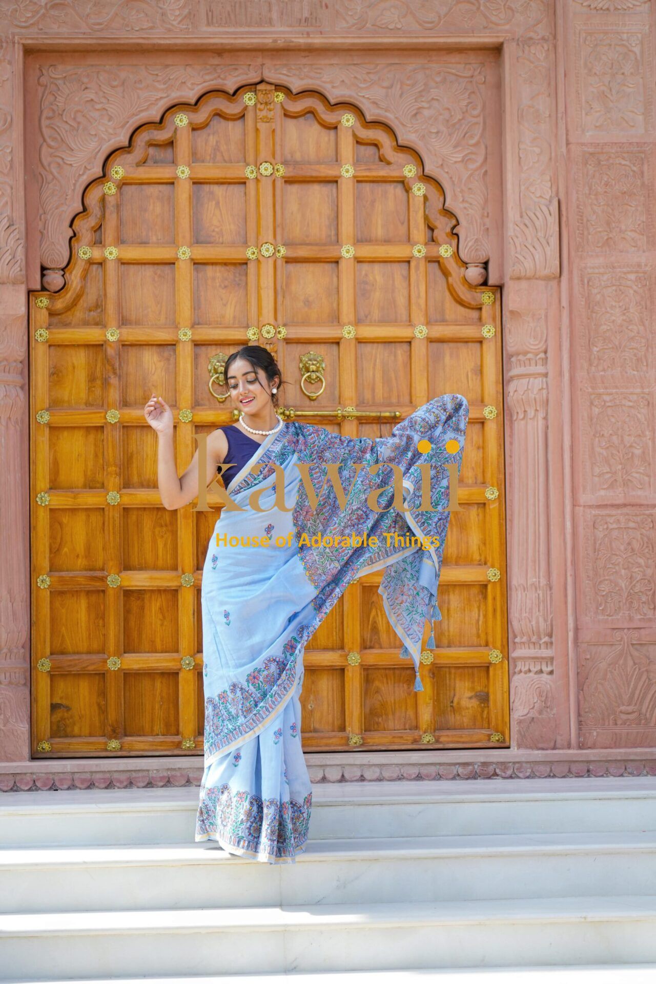 Woman wearing blue madhubani saree by Kawaii standing in front of ornate wooden door