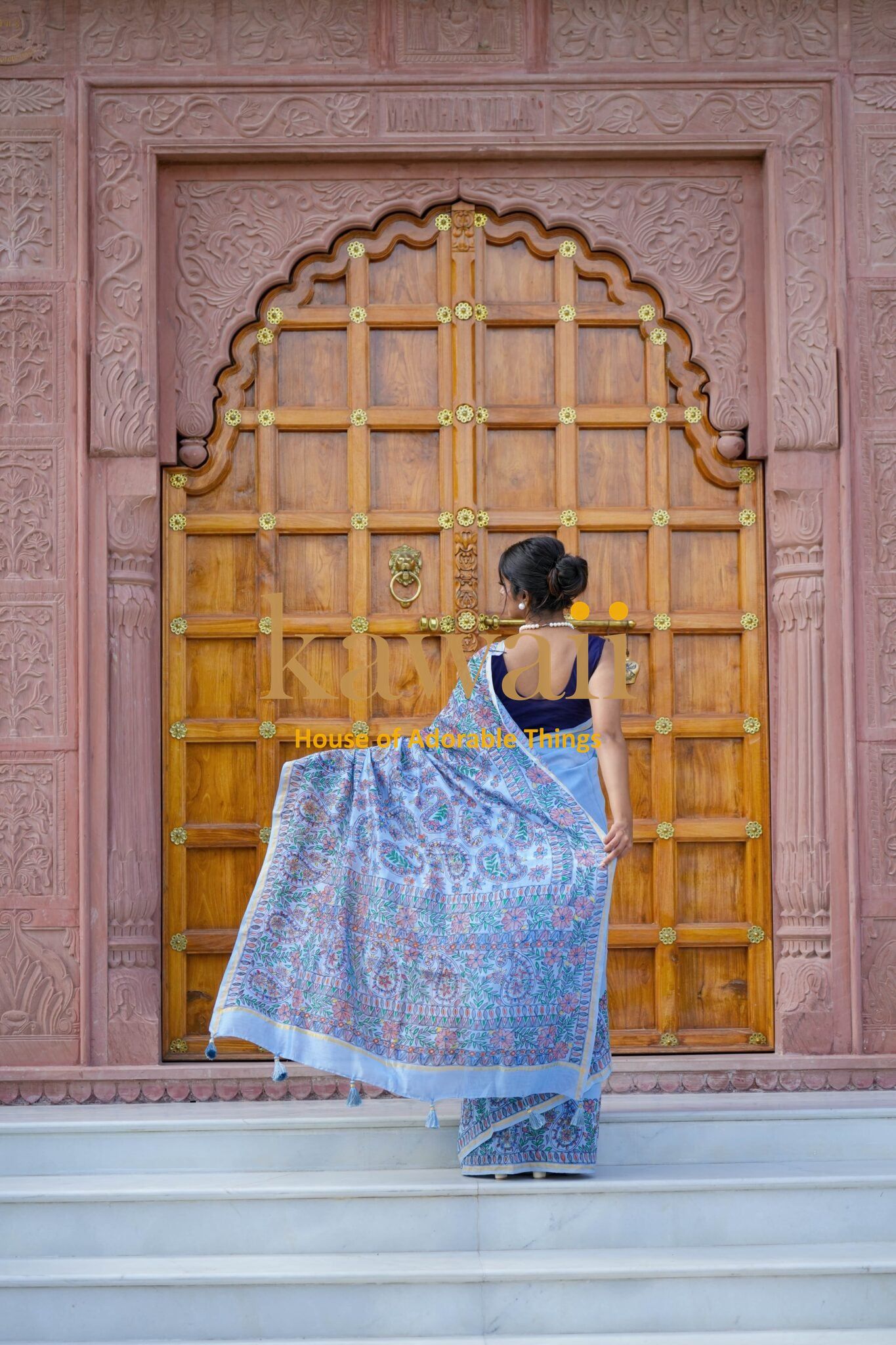 Woman wearing a colorful Madhubani saree by Kawaii standing in front of an ornate wooden door