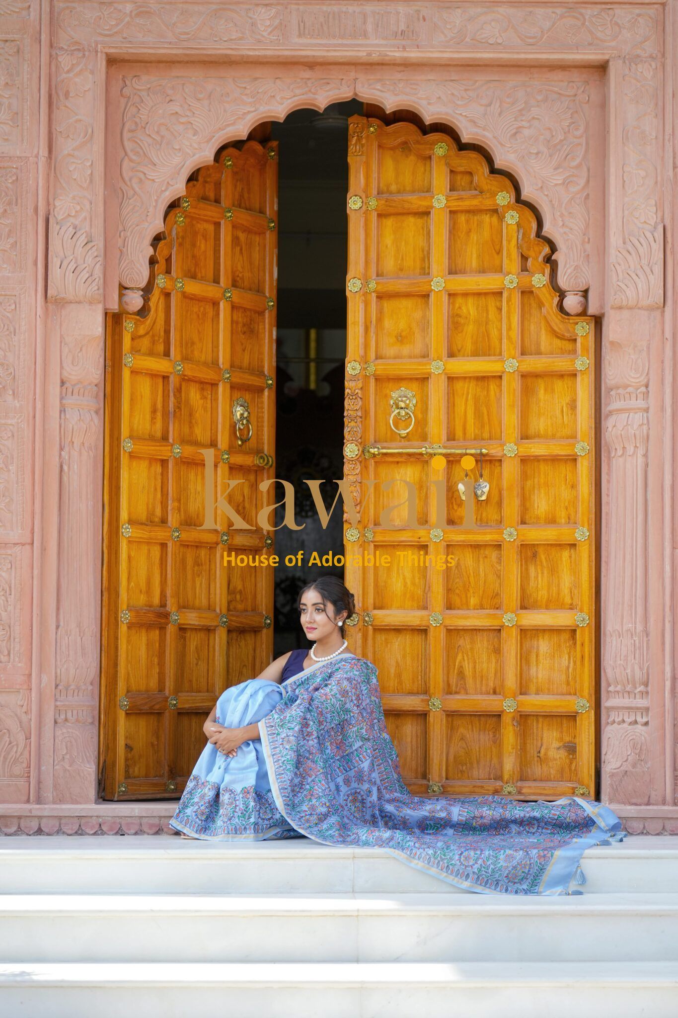 Woman sitting on steps wearing a blue and purple madhubani saree with traditional Indian patterns