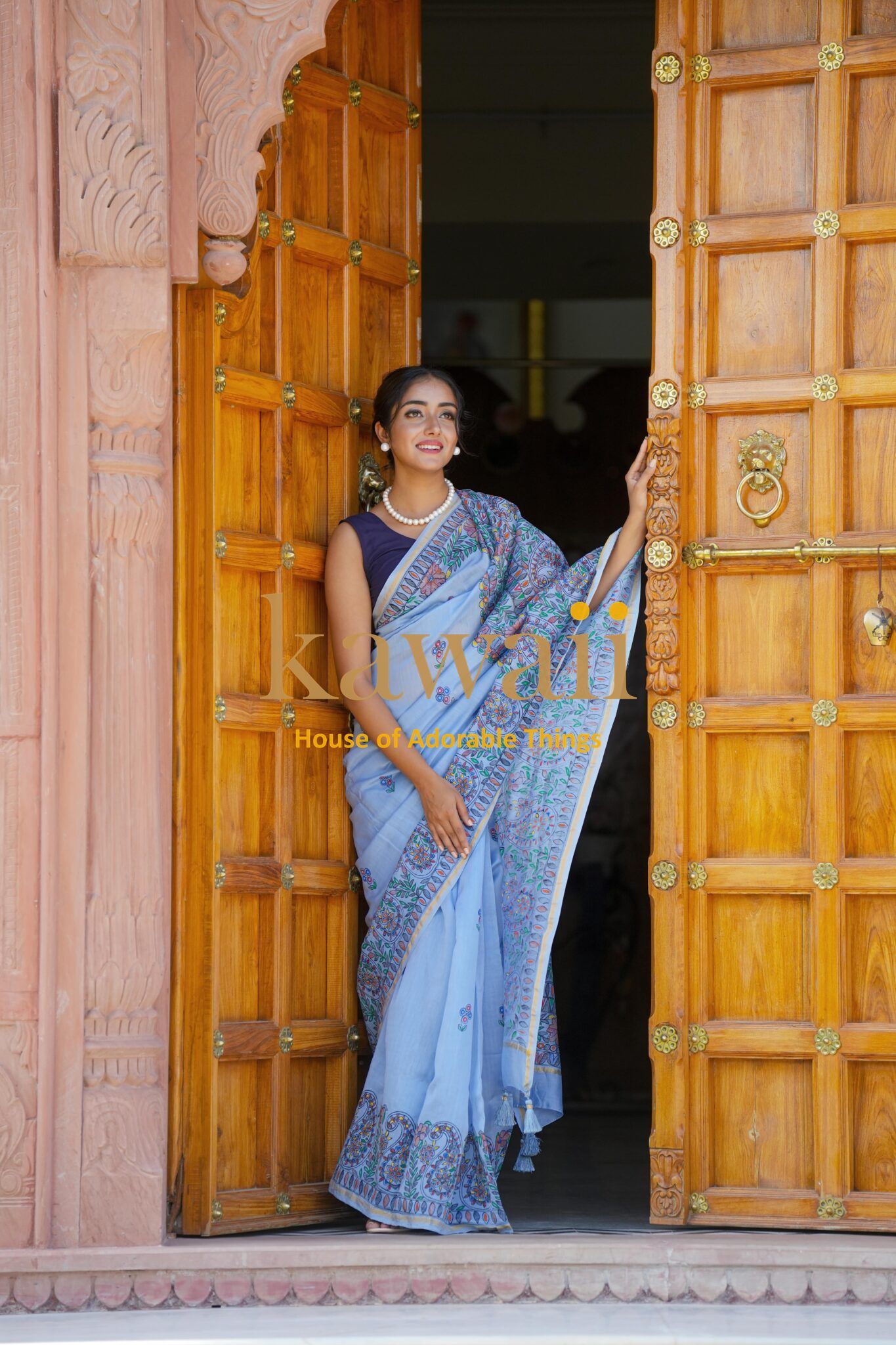 Woman wearing a blue madhubani saree standing by traditional wooden carved doors