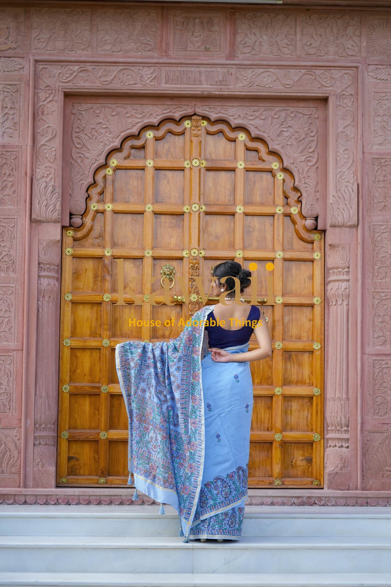 Woman wearing Kawaii madhubani saree with intricate traditional patterns standing in front of a carved wooden door