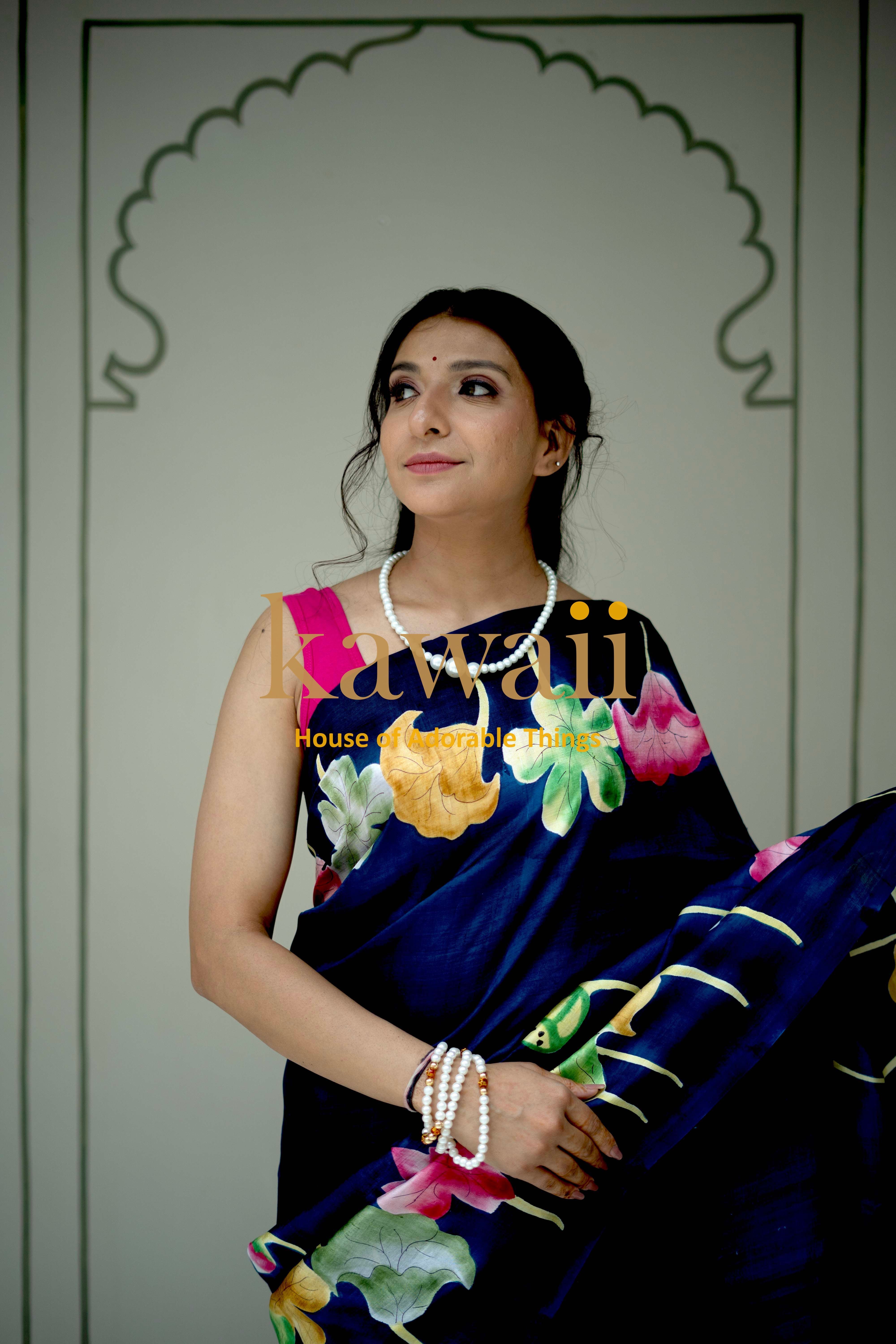 Kawaii pichwai saree in navy blue with colorful floral prints worn by woman with pearl jewelry