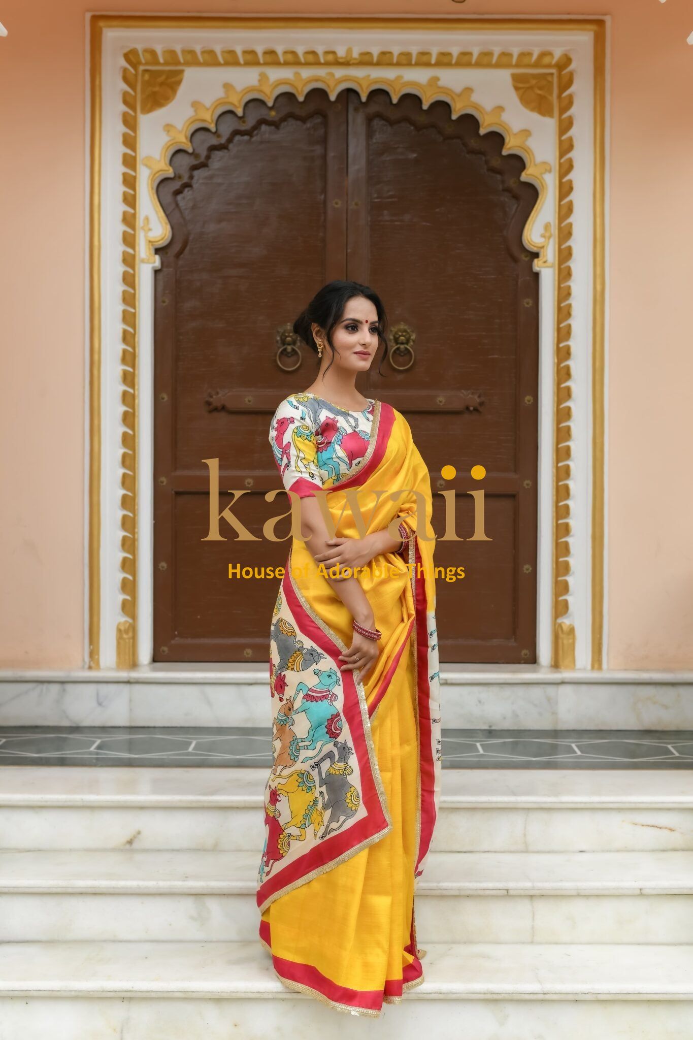 Kawaii yellow pichwai saree with colorful traditional motifs worn by woman in front of ornate wooden door