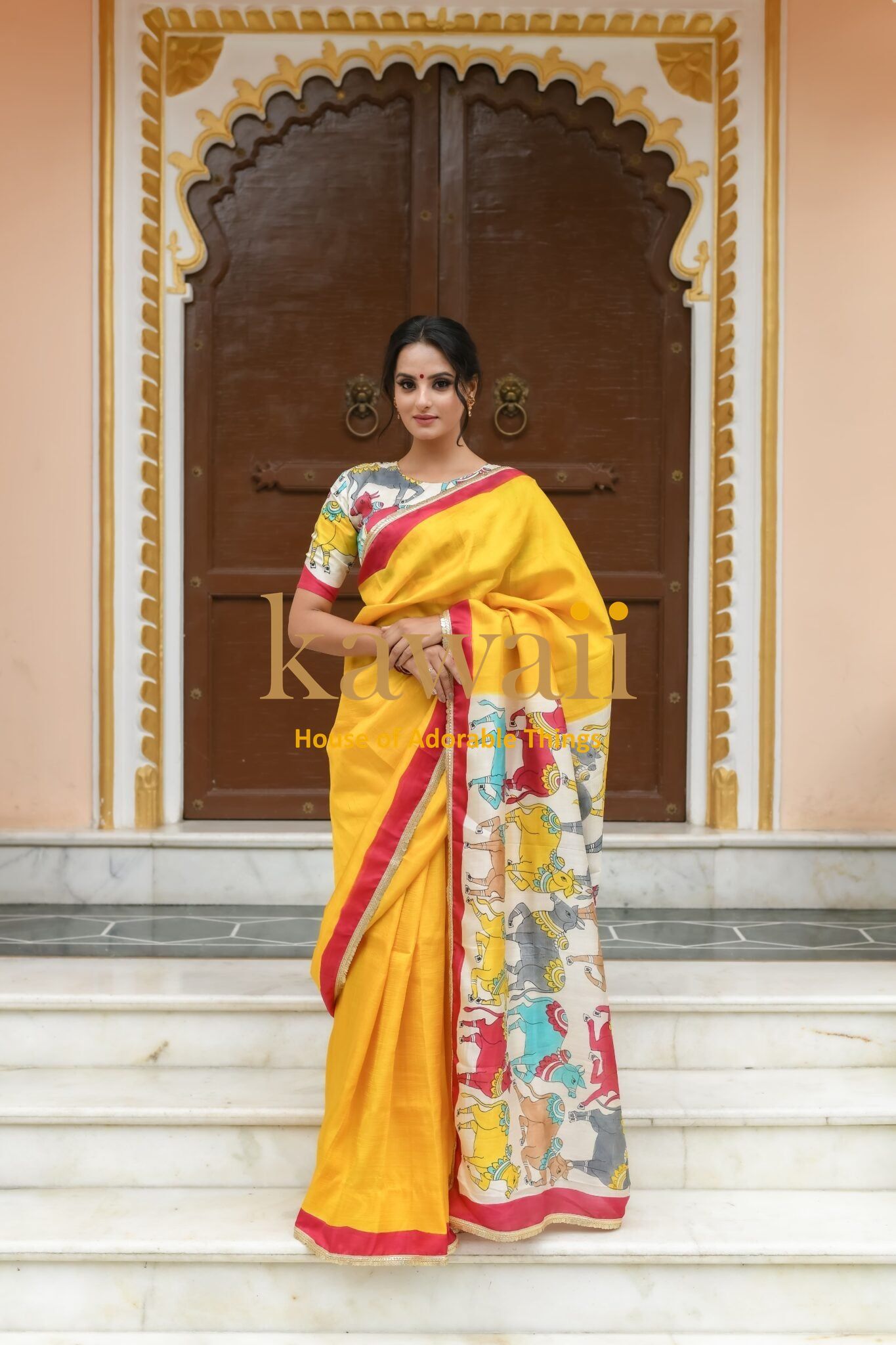 Kawaii yellow pichwai saree with multi-colored traditional design worn by woman standing on marble steps