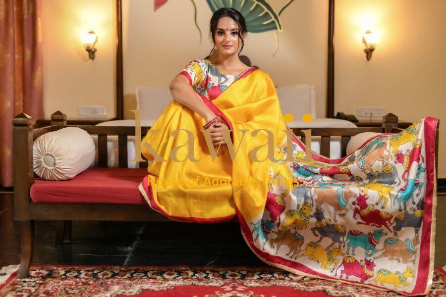 Kawaii yellow pichwai saree with colorful traditional animal motifs worn by woman sitting on wooden sofa