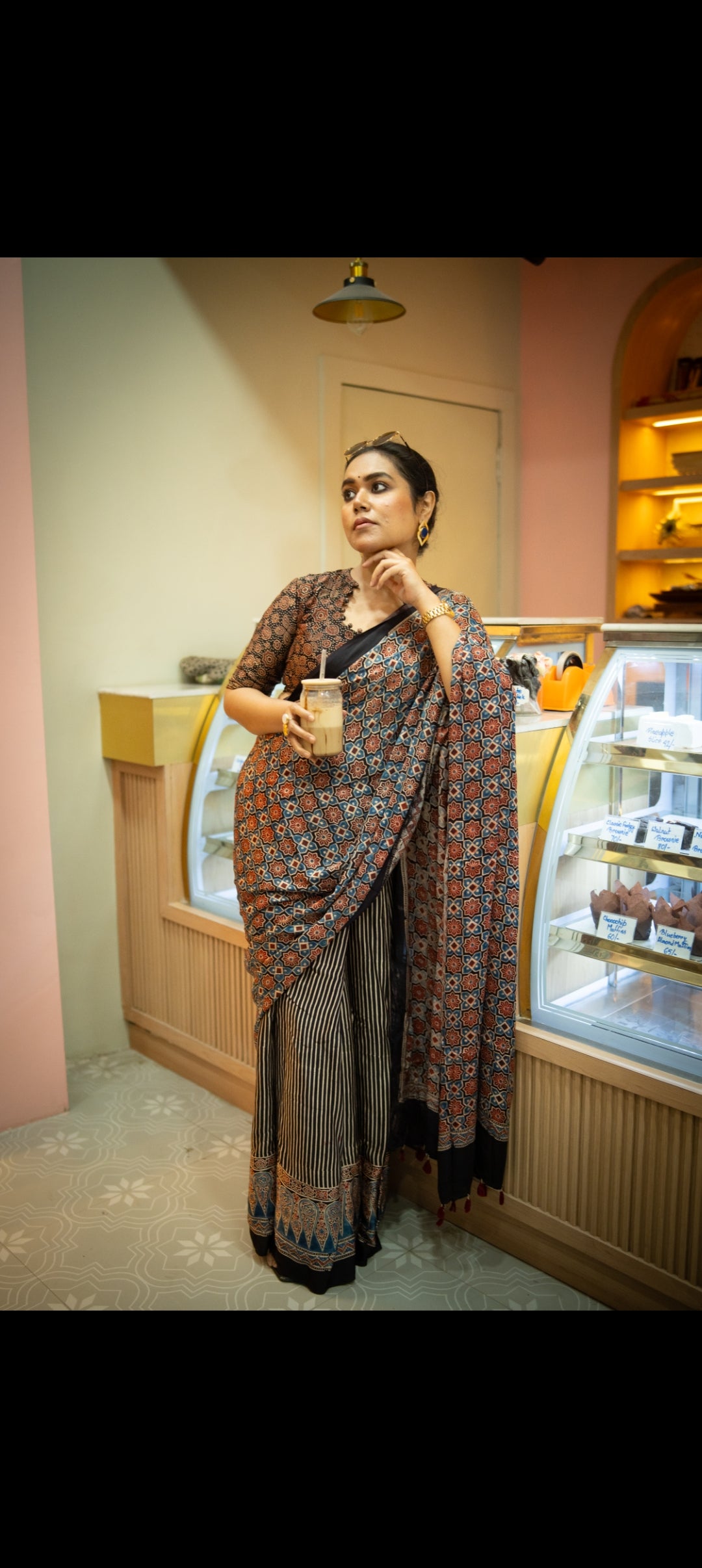 Woman wearing best authentic ajrakh saree by Kawaii holding a drink in a cafe setting