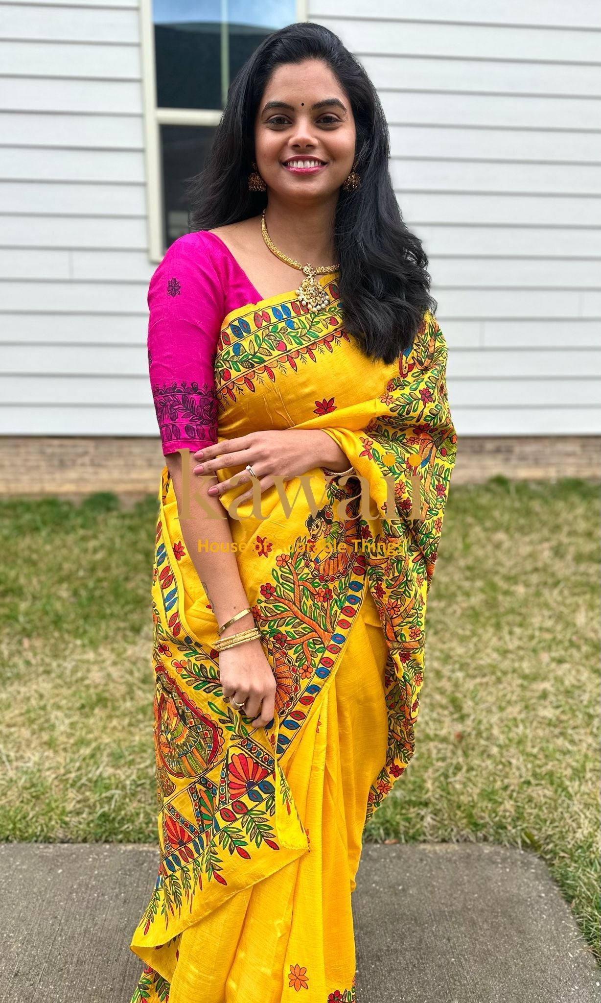 Woman wearing a bright yellow madhubani saree with traditional floral patterns and pink blouse outdoors