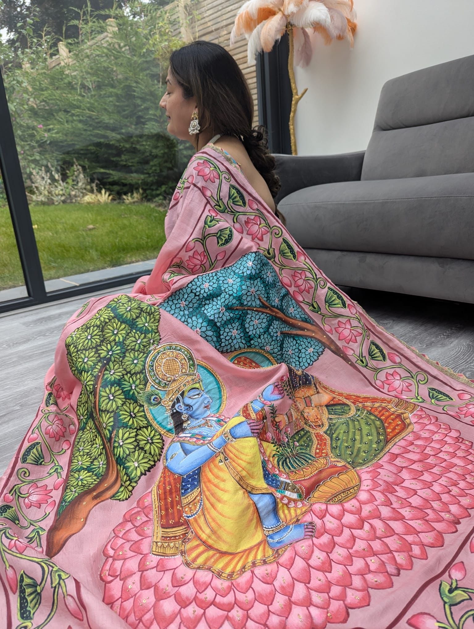 Woman wearing a pink pichwai saree with intricate traditional artwork featuring a deity and floral designs