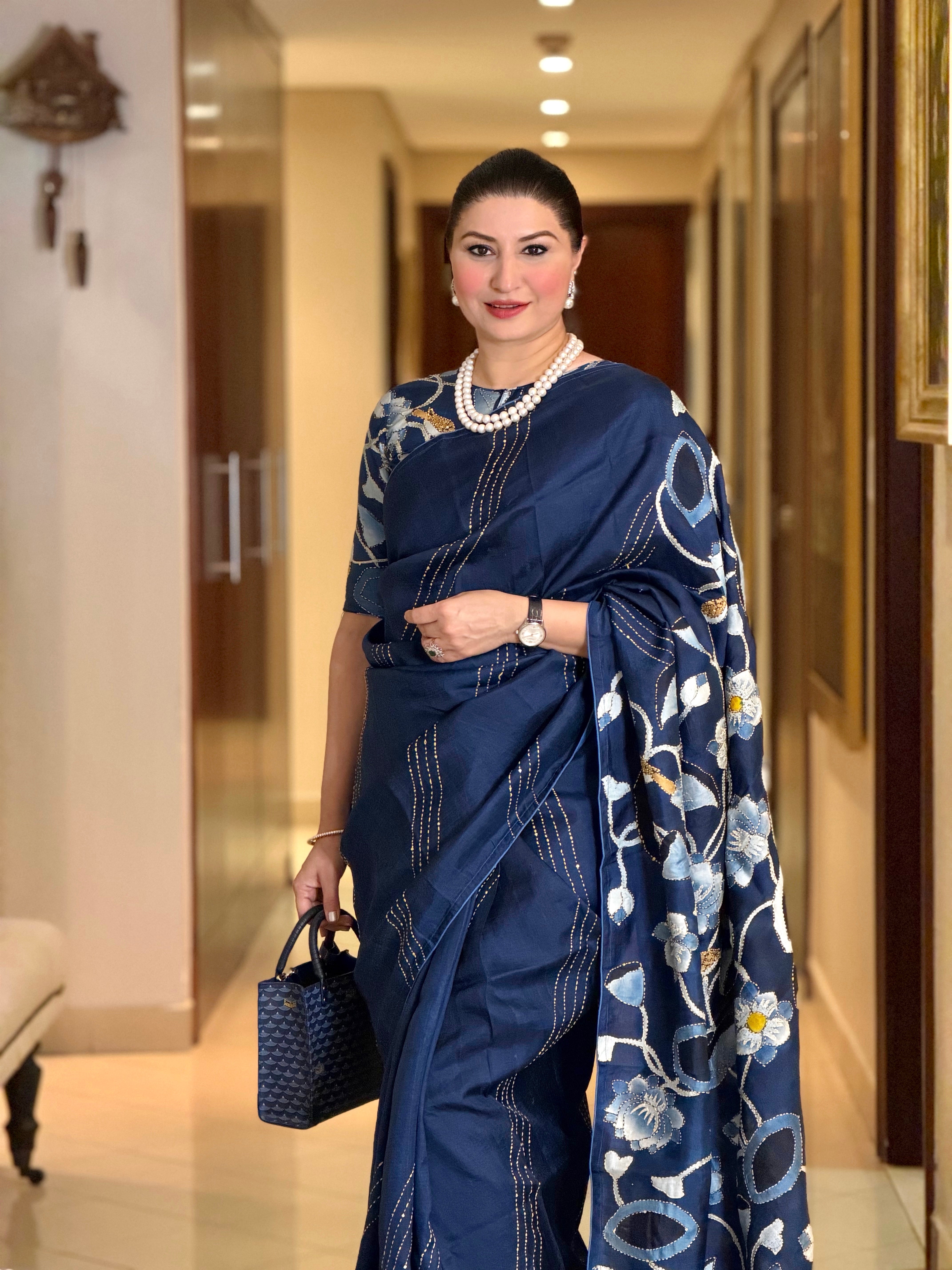 Elegant woman wearing a stunning pichwai saree with floral designs, accessorized with pearls and a handbag