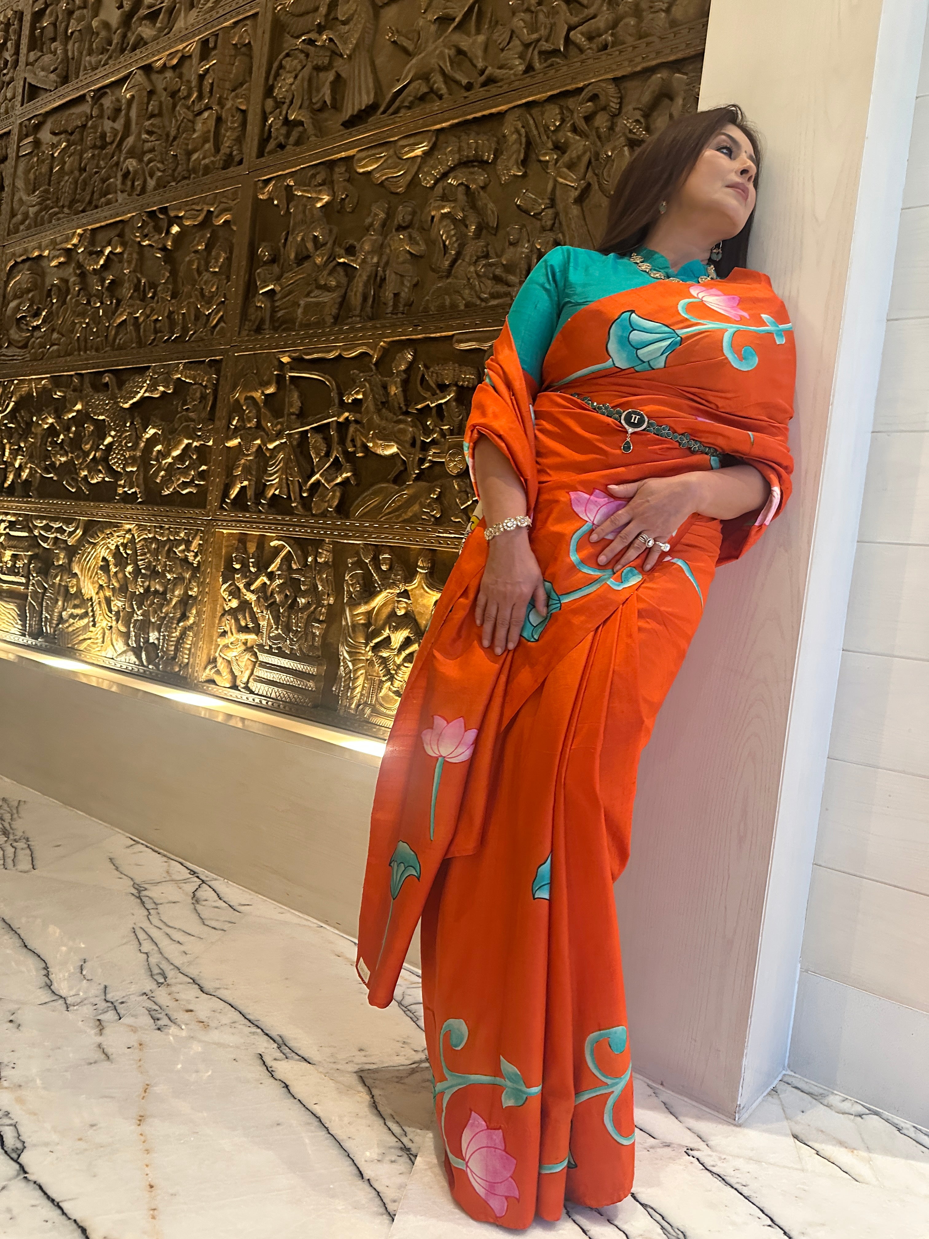 Vibrant Pichwai Saree in orange with floral motifs, elegantly draped for festive occasions