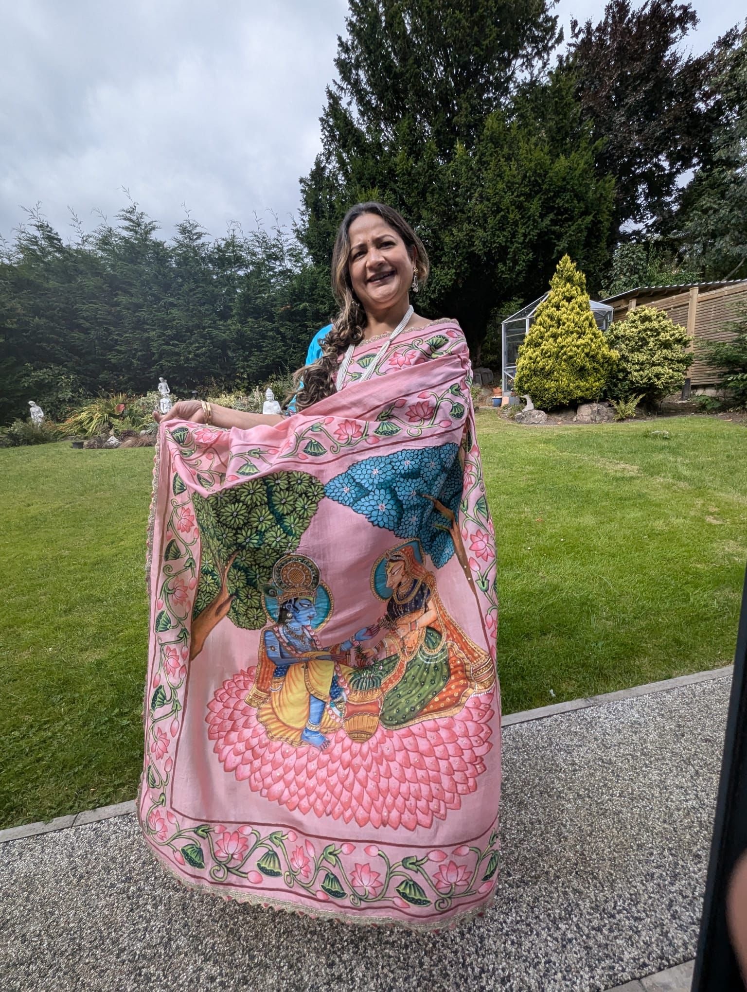 Woman wearing a pink pichwai saree with intricate traditional Indian artwork in a garden setting