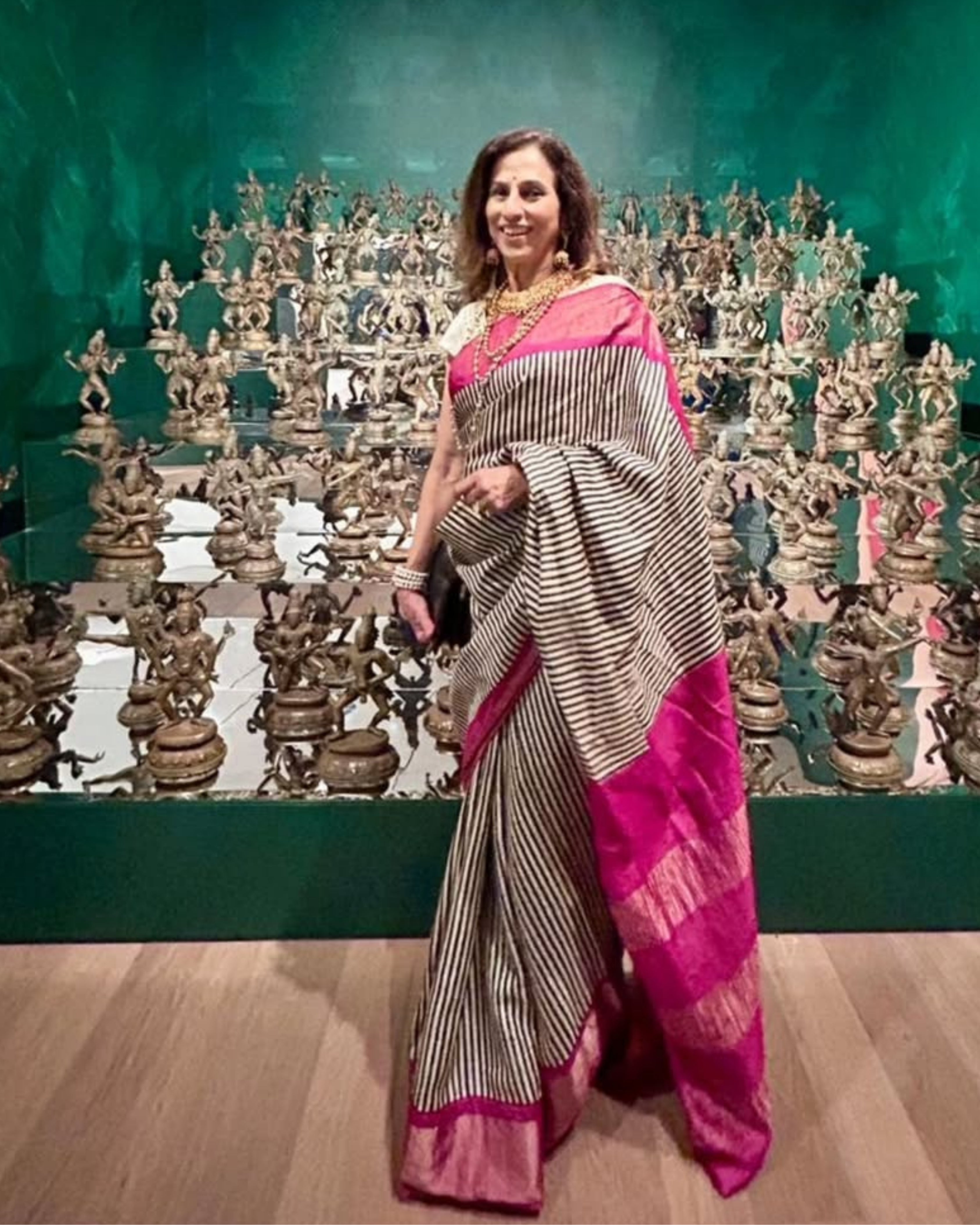 Woman in a striped tussar silk saree with pink border, showcased against intricate bronze sculptures