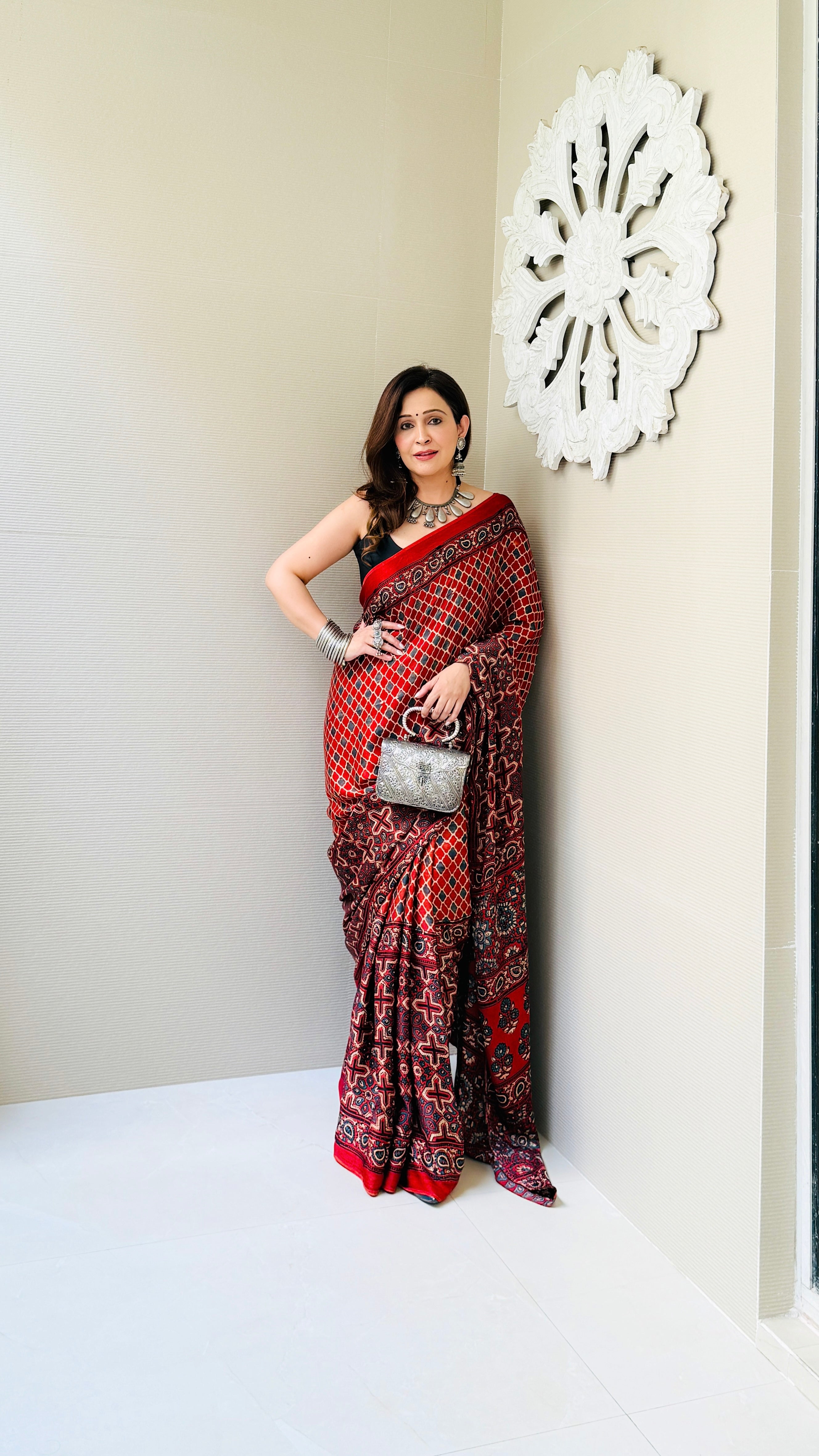 Woman wearing red and black ajrakh saree with geometric patterns holding a silver handbag