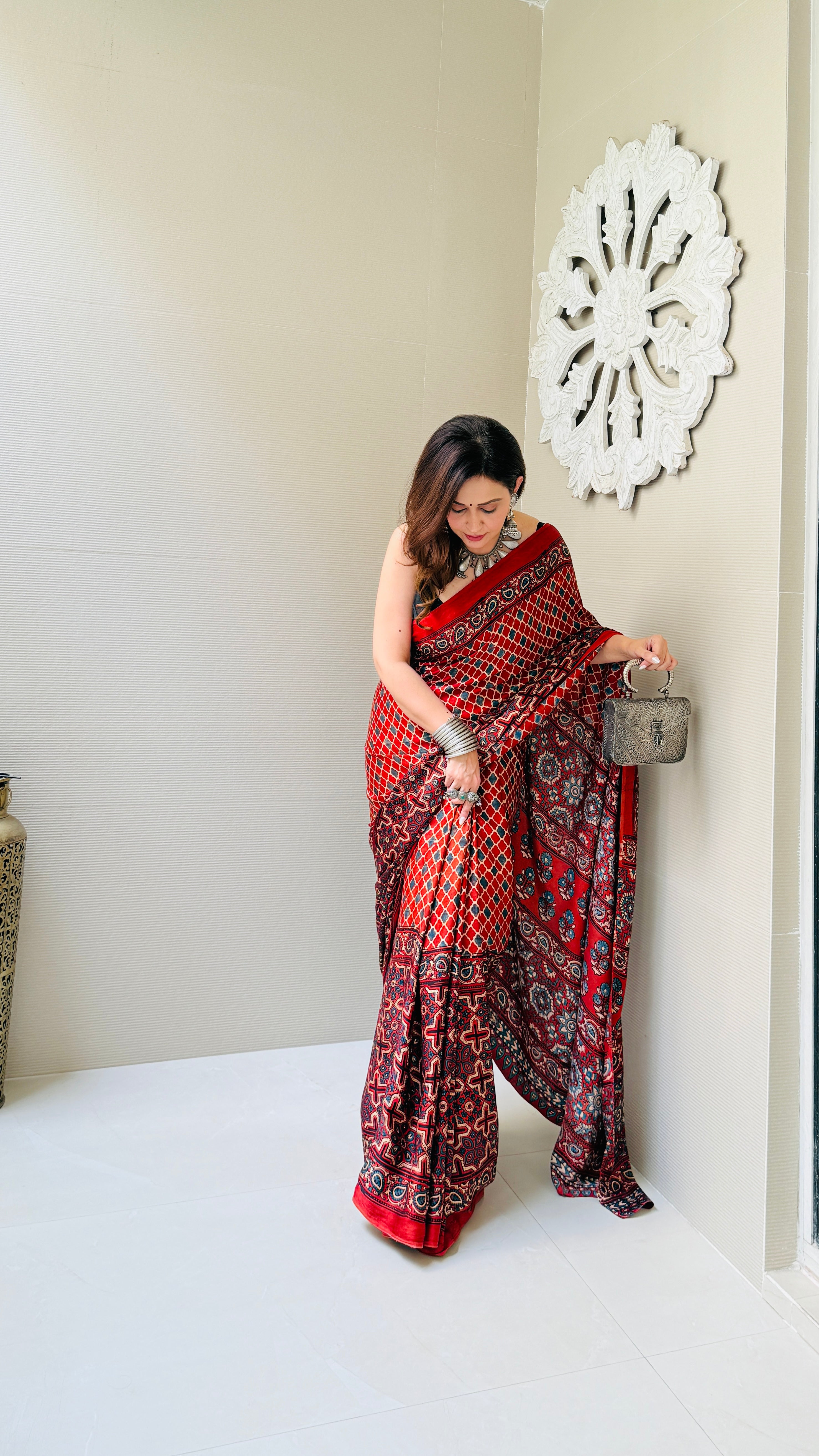 Woman wearing a red and black ajrakh saree by Kawaii holding a small handbag indoors